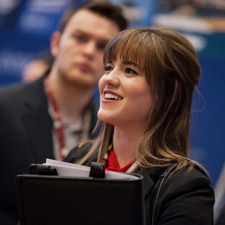 A young woman holding a portfolio smiles.