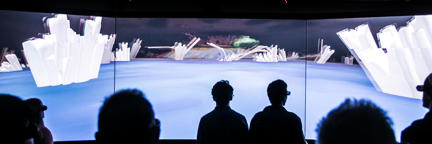 People are silhouetted as they look at 3D imagery on a virtual reality wall.