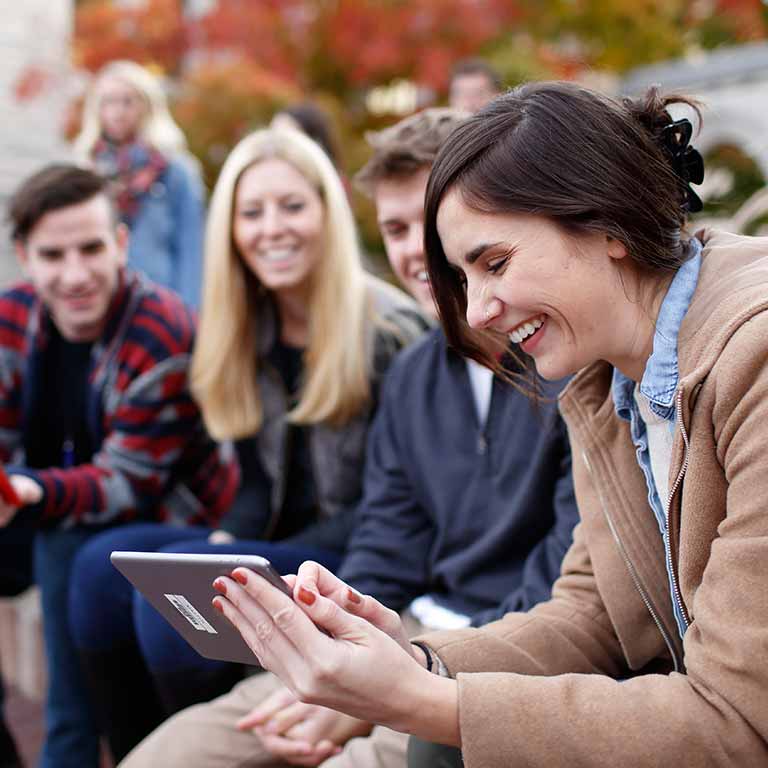A group of young men and women smile as they look at a tablet computer.